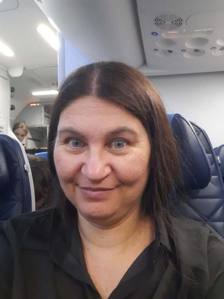 Karen seated in the cabin of a LOT Polish Airlines flight, travelling with a dog.