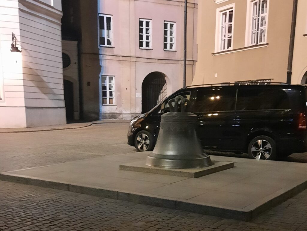 The Wishing Bell in Canon Square in Warsaw Old Town next to a van to show how big the wishing bell is